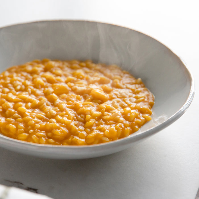 Close-up of butternut squash risotto in a shallow white bowl, creamy glossy orange rice on a light background