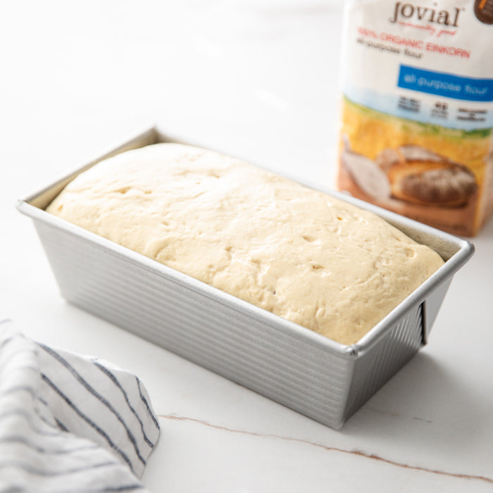 Angled view of risen Einkorn dough in a metal loaf pan showing a fluffy no-knead rise with a Jovial flour bag in background