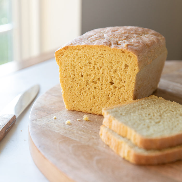 Front view of a sliced Einkorn loaf showcasing a tender golden crumb on a wooden cutting board by a window