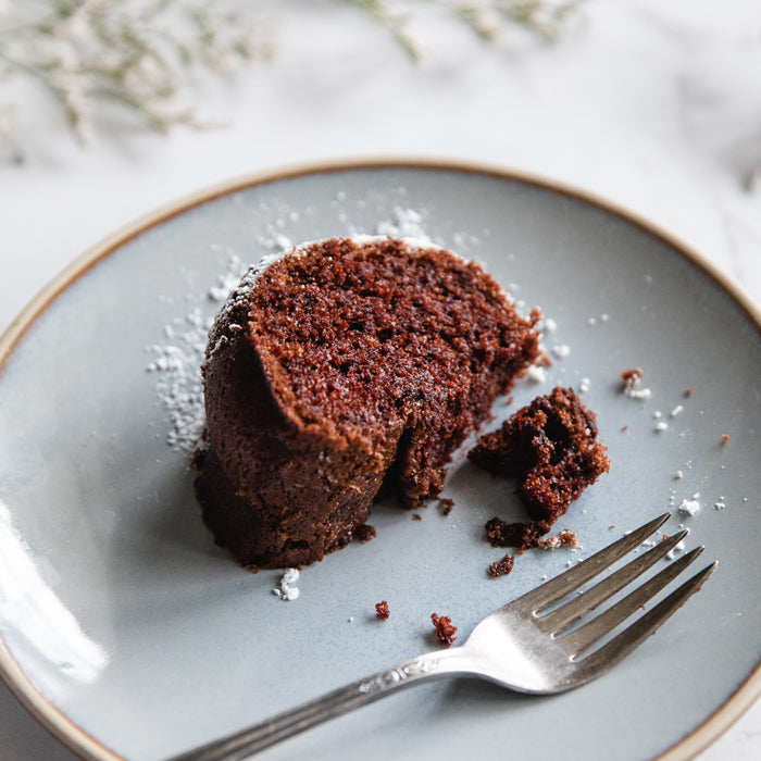 Close-up of a partially eaten dairy-free chocolate olive oil Bundt cake slice showing moist crumb and powdered sugar on a gray plate with a fork