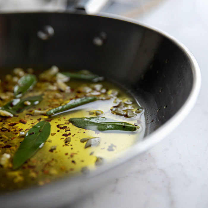 Skillet of olive oil gently simmering with sage leaves, garlic slices, and red pepper flakes for Fusilli Aglio-Olio