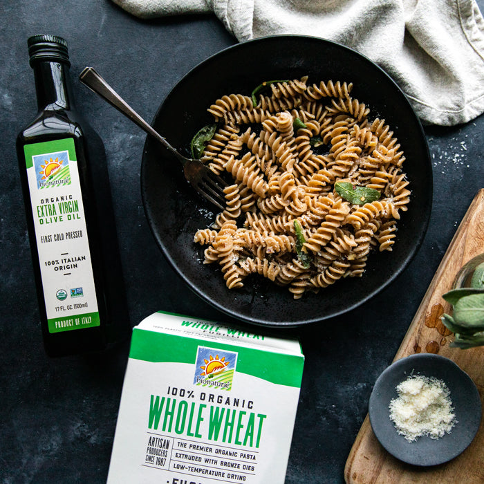 Bowl of whole-wheat fusilli with sage and cheese beside bottle of organic olive oil and a 100 percent organic pasta box