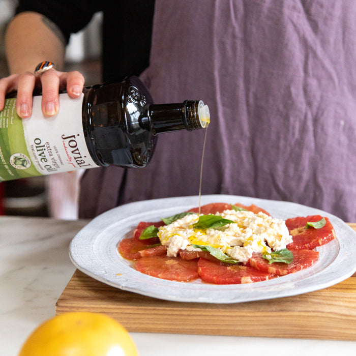 Person pouring Jovial extra virgin olive oil over grapefruit and burrata salad with basil on a plate