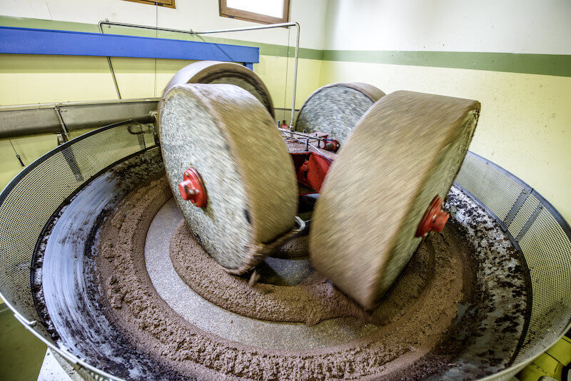Stone millstones grinding olive paste in a small Italian olive mill, showing traditional pressing equipment