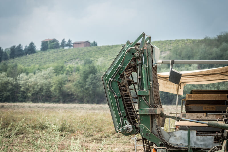 Green tomato harvester parked in an organic field with rolling hills and a farmhouse in the distance
