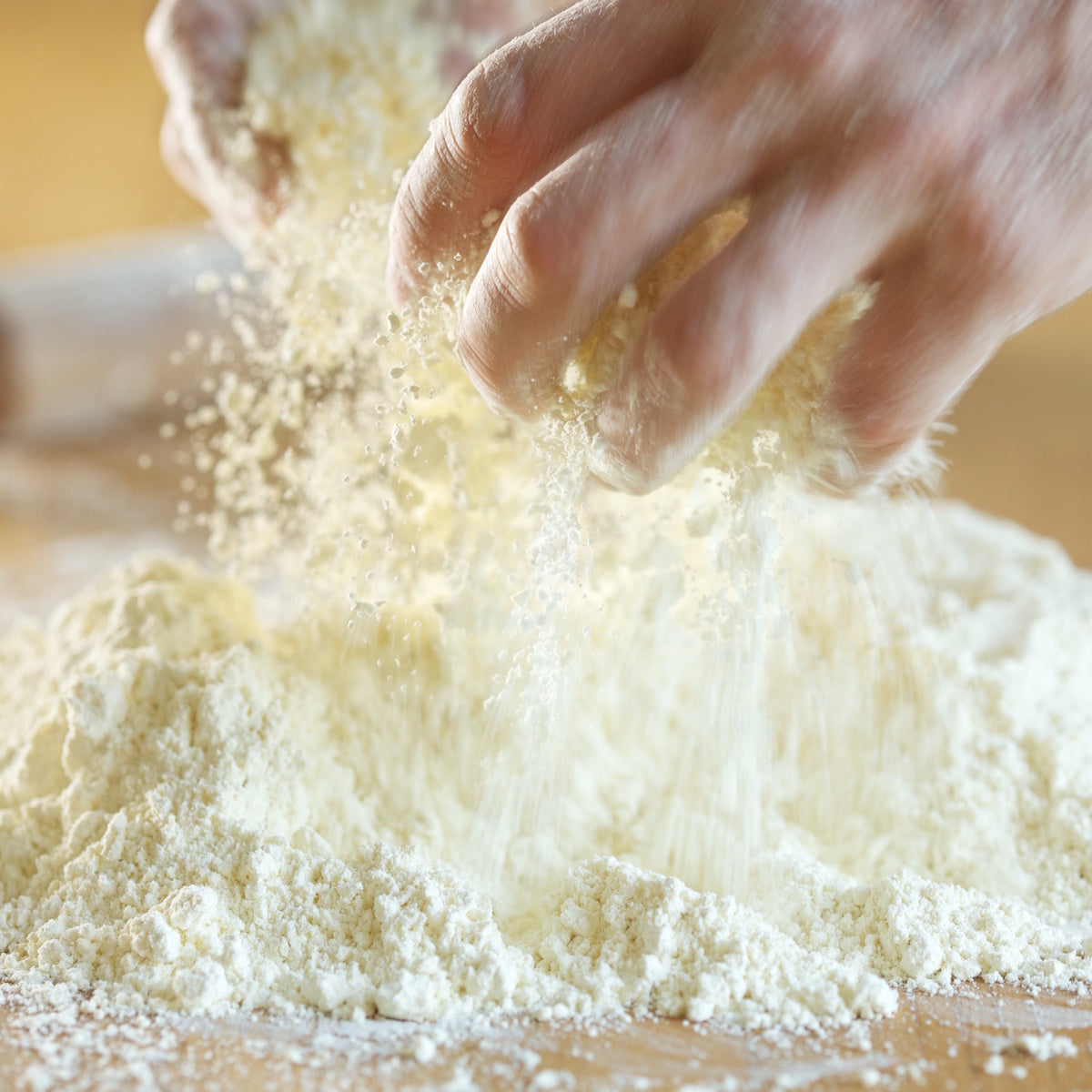 Hands sprinkling organic einkorn flour onto a wooden work surface for baking