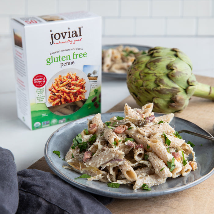 Bowl of artichoke penne with creamy sauce and crispy pancetta, Jovial gluten-free brown rice penne box and artichoke behind