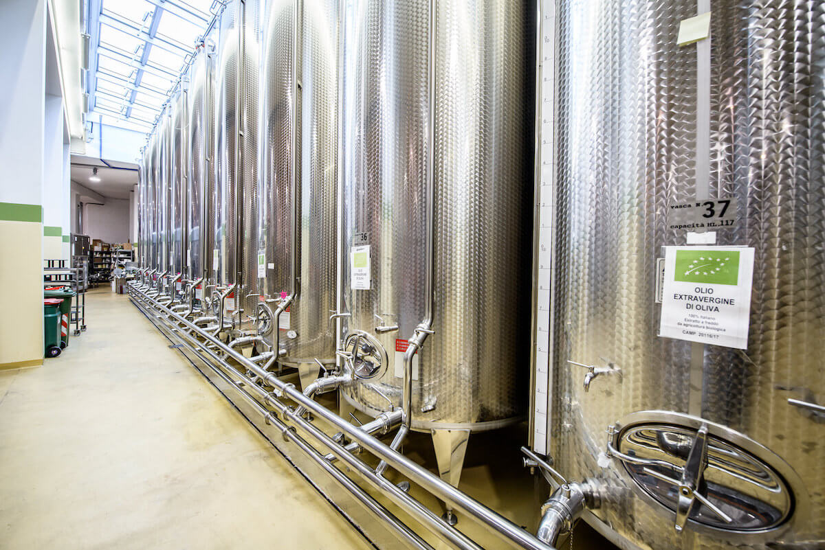 Row of stainless-steel olive oil tanks in a bright Italian pressing and bottling facility