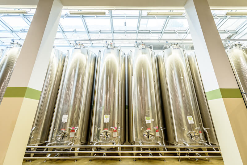 Row of tall stainless steel olive oil storage tanks inside a bright Italian pressing and bottling facility