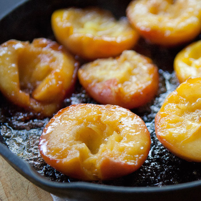 Caramelized peach halves sizzling in a cast-iron skillet with glossy caramel juices