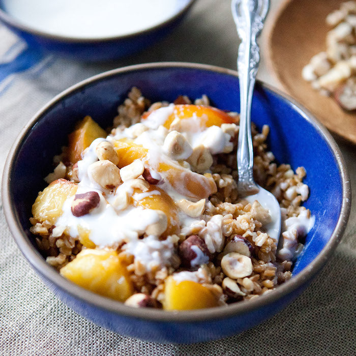 Caramelized peach and einkorn wheat berry breakfast bowl topped with yogurt and toasted hazelnuts in a blue bowl