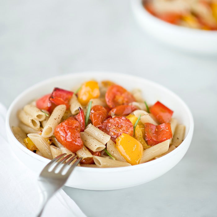 Bowl of Einkorn penne tossed with oven-roasted cherry tomatoes and red and yellow peppers, fork resting on bowl edge