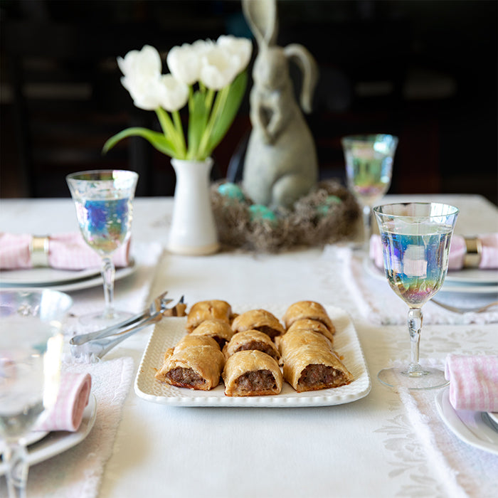 Plate of baked Einkorn sausage rolls on a dressed dining table with tulips and iridescent wine glasses