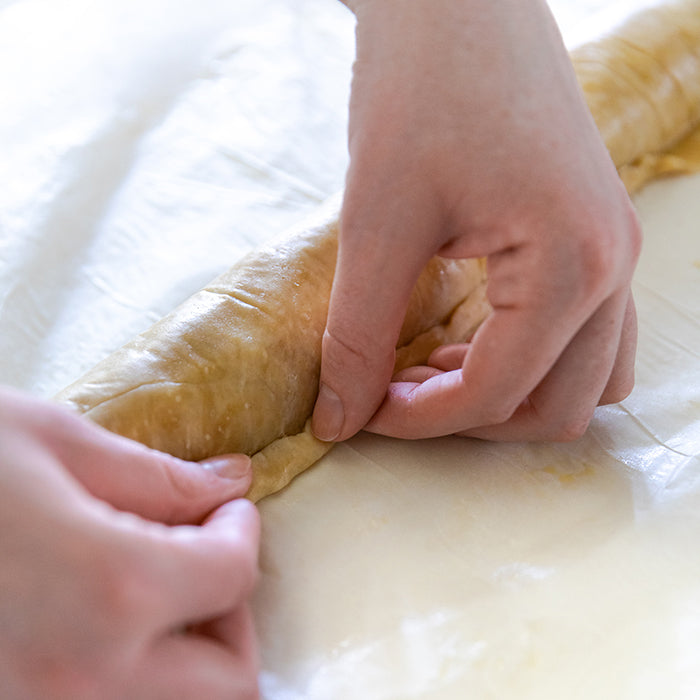 Hands sealing rolled einkorn sausage roll on parchment before baking