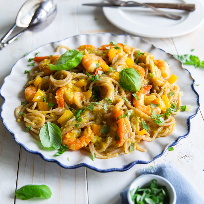 Plate of Mediterranean-style shrimp pasta made with cassava noodles and diced yellow pepper, garnished with basil on a white wooden table