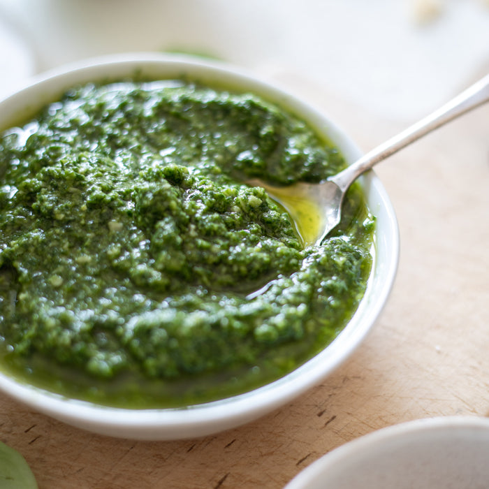 Close-up of a bowl of fresh basil pesto showing chunky texture and olive oil sheen on a wooden cutting board