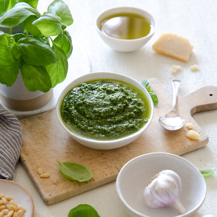 Bowl of fresh basil pesto on a wooden cutting board with basil leaves, garlic, olive oil, parmesan, and pine nuts