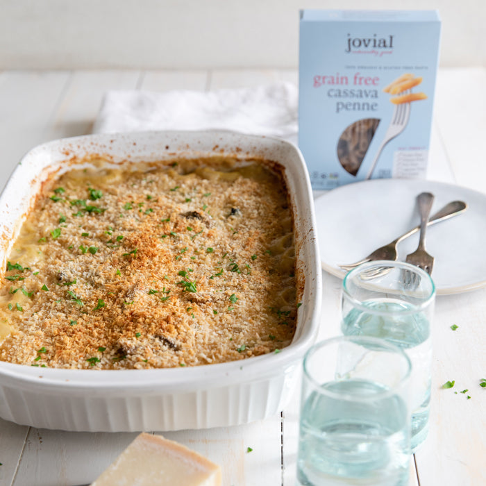 Front view of baked cassava penne in a casserole showcasing golden breadcrumb topping with Jovial grain-free penne box behind
