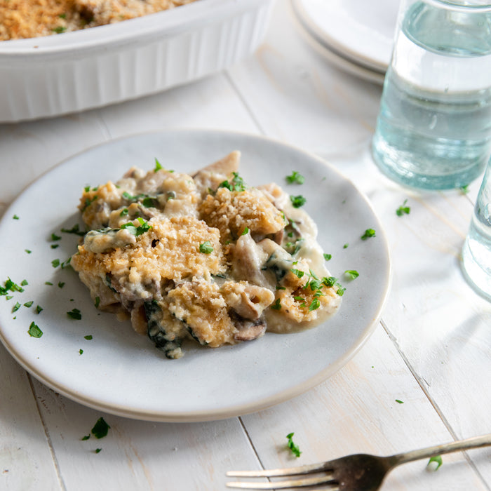 Angled view of baked penne with creamy cauliflower sauce, kale, mushrooms and golden breadcrumb topping on a white plate