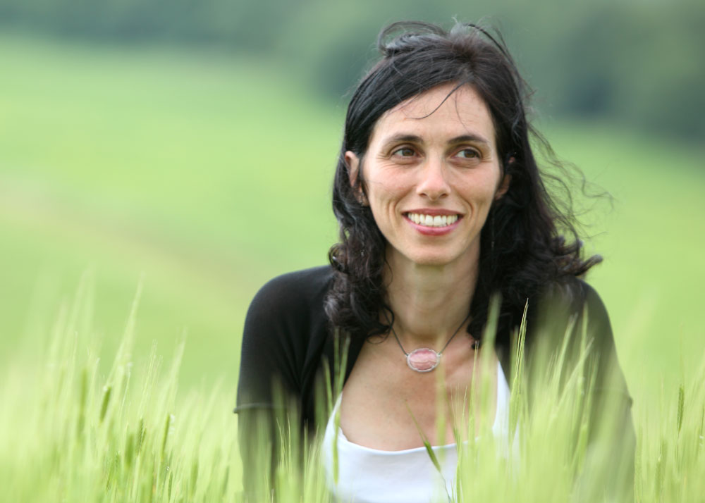 Smiling woman sitting among tall einkorn wheat in a sunlit field