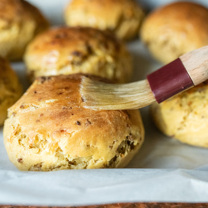 Einkorn dinner rolls with sausage and cheese being brushed with melted butter on a parchment-lined baking tray