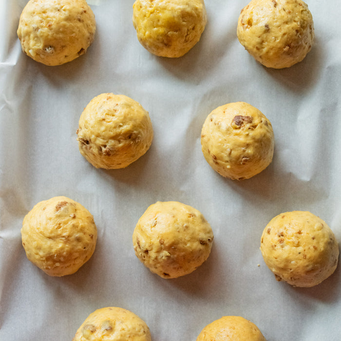 Overhead view of uncooked Einkorn dinner roll dough balls with sausage and cheese on a parchment-lined baking sheet