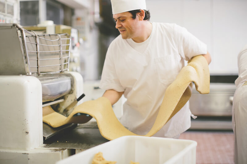 Baker stretching traditional Italian sourdough cracker dough on a sheeter in an artisan commercial kitchen