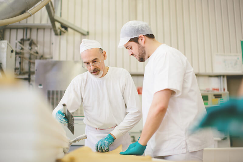 Two bakers shaping sourdough cracker dough in a small artisan bakery production area
