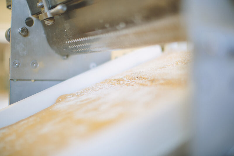 Sourdough cracker dough moving on a conveyor belt under bakery machinery in a small artisan family bakery