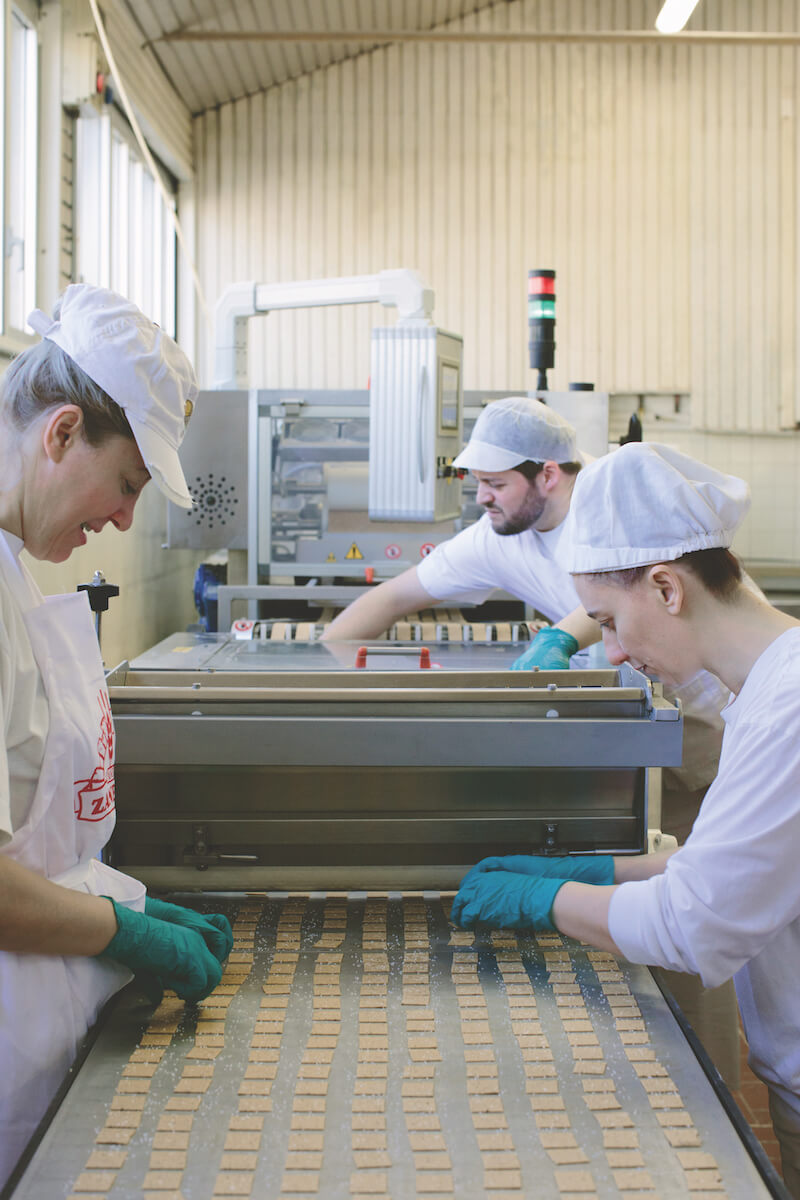 Three bakery workers placing and inspecting rows of sourdough crackers on a conveyor belt in an artisan production kitchen