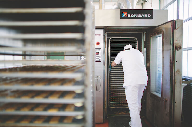 Bakery worker loading racks of sourdough crackers into a Bongard industrial oven in an artisan bakery