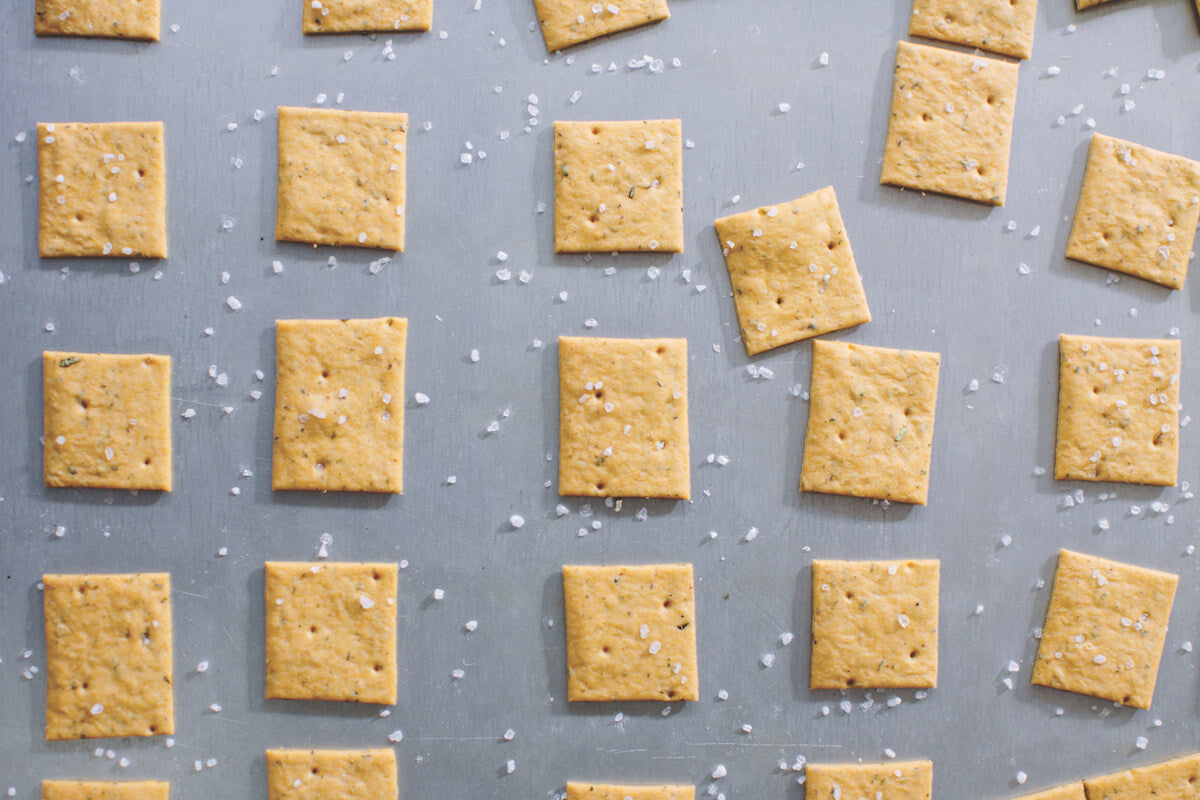 Top-down view of sourdough einkorn crackers showcasing sea salt and flecked grains on a gray baking sheet