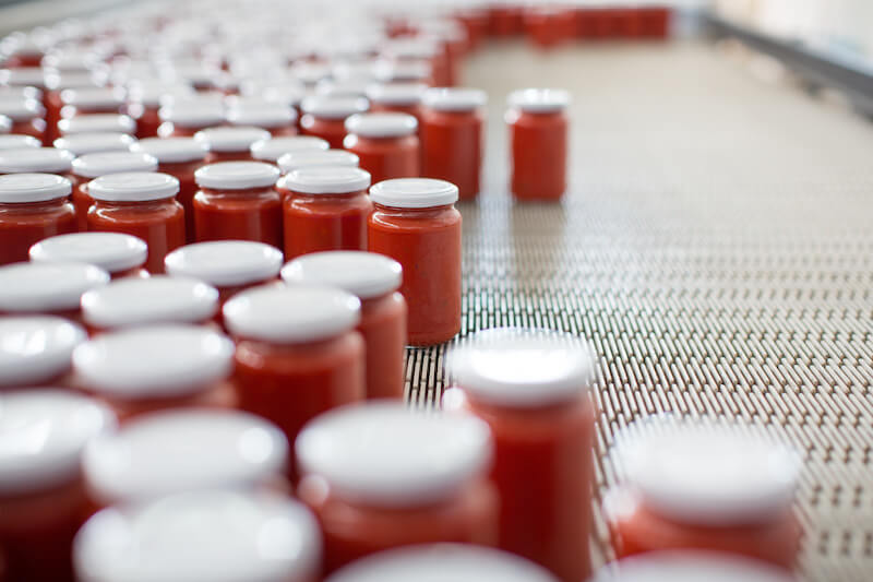 Rows of glass jars of organic crushed tomatoes moving on a conveyor belt in an Italian factory