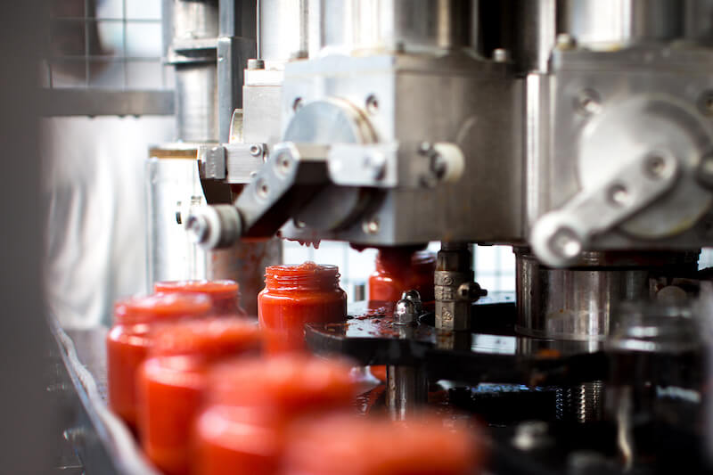 Jars of organic tomato sauce being filled on an automated assembly line in a traditional Italian factory