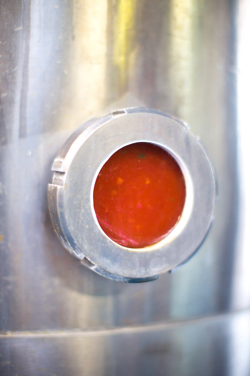 Tomato sauce visible through a stainless-steel tank sight glass during packing at an organic Italian canning facility