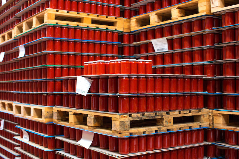 Stacks of jars of organic crushed tomatoes on wooden pallets in a traditional Italian production facility