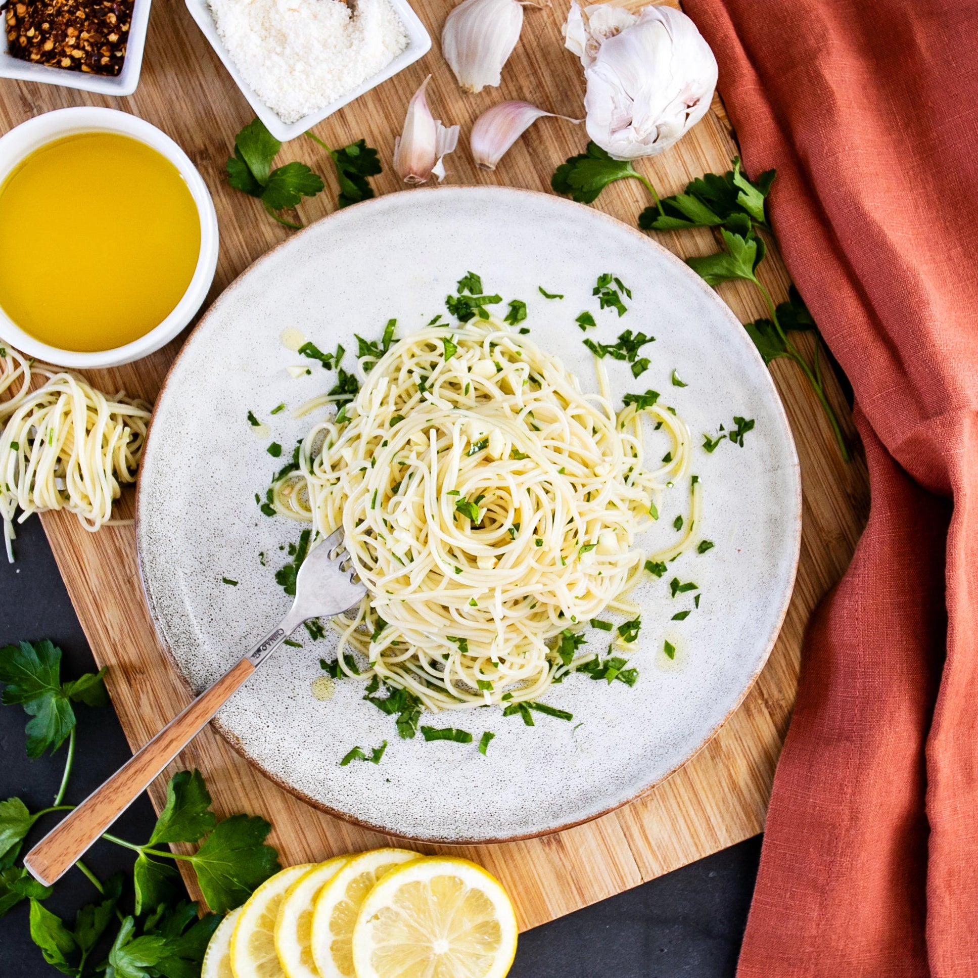 Organic capellini twirled into a nest with olive oil, lemon, parsley, and garlic on a ceramic plate over a wooden board