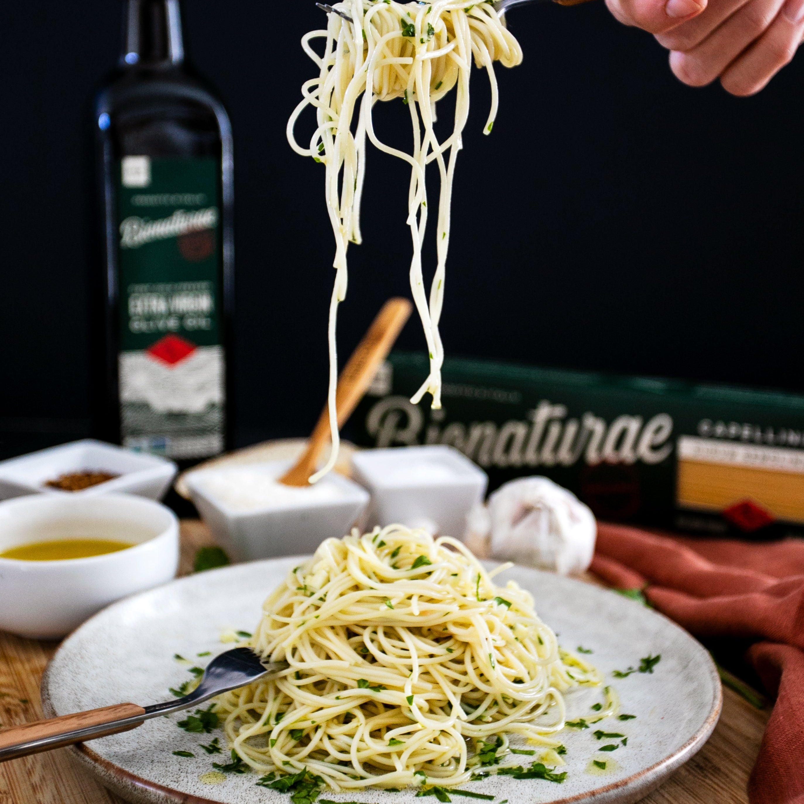 Cooked organic capellini being twirled with a fork over a plated serving, olive oil bottle and bionaturae box blurred in the background