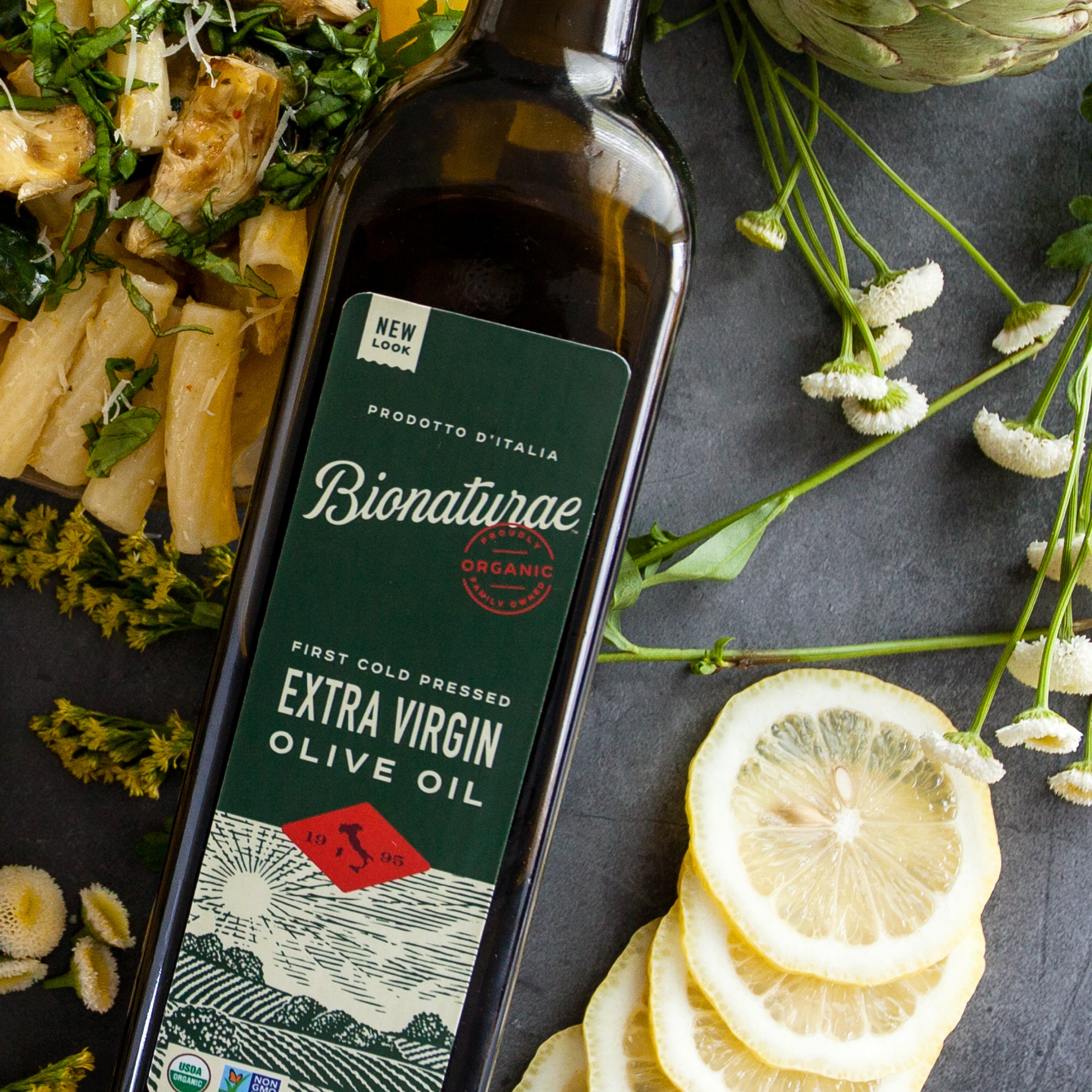 Bottle of Bionaturae organic extra virgin olive oil beside sliced lemons and fresh herbs on a dark surface
