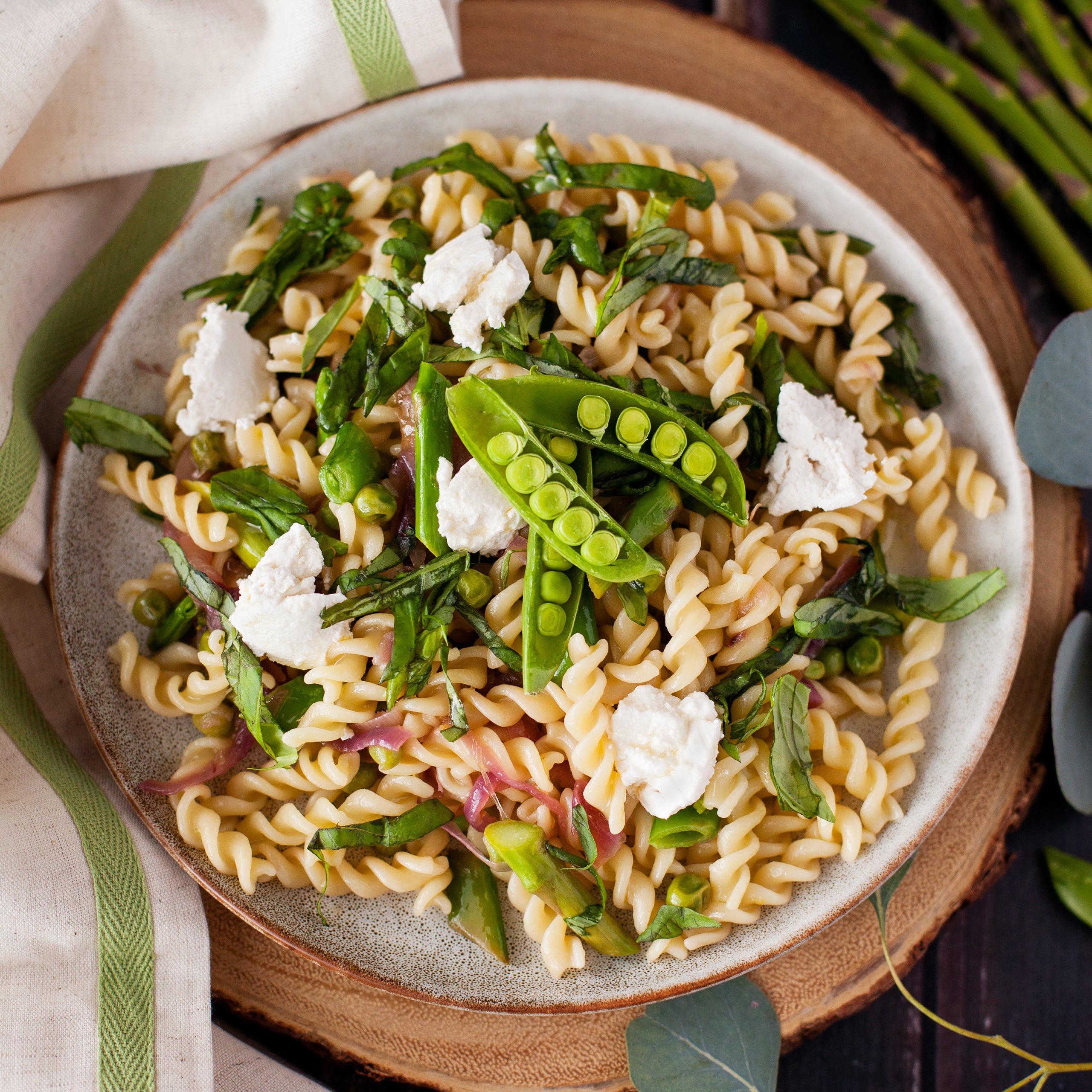 Top-down view of organic durum semolina fusilli showcasing corkscrew pasta tossed with peas, asparagus, basil, and ricotta on a ceramic plate
