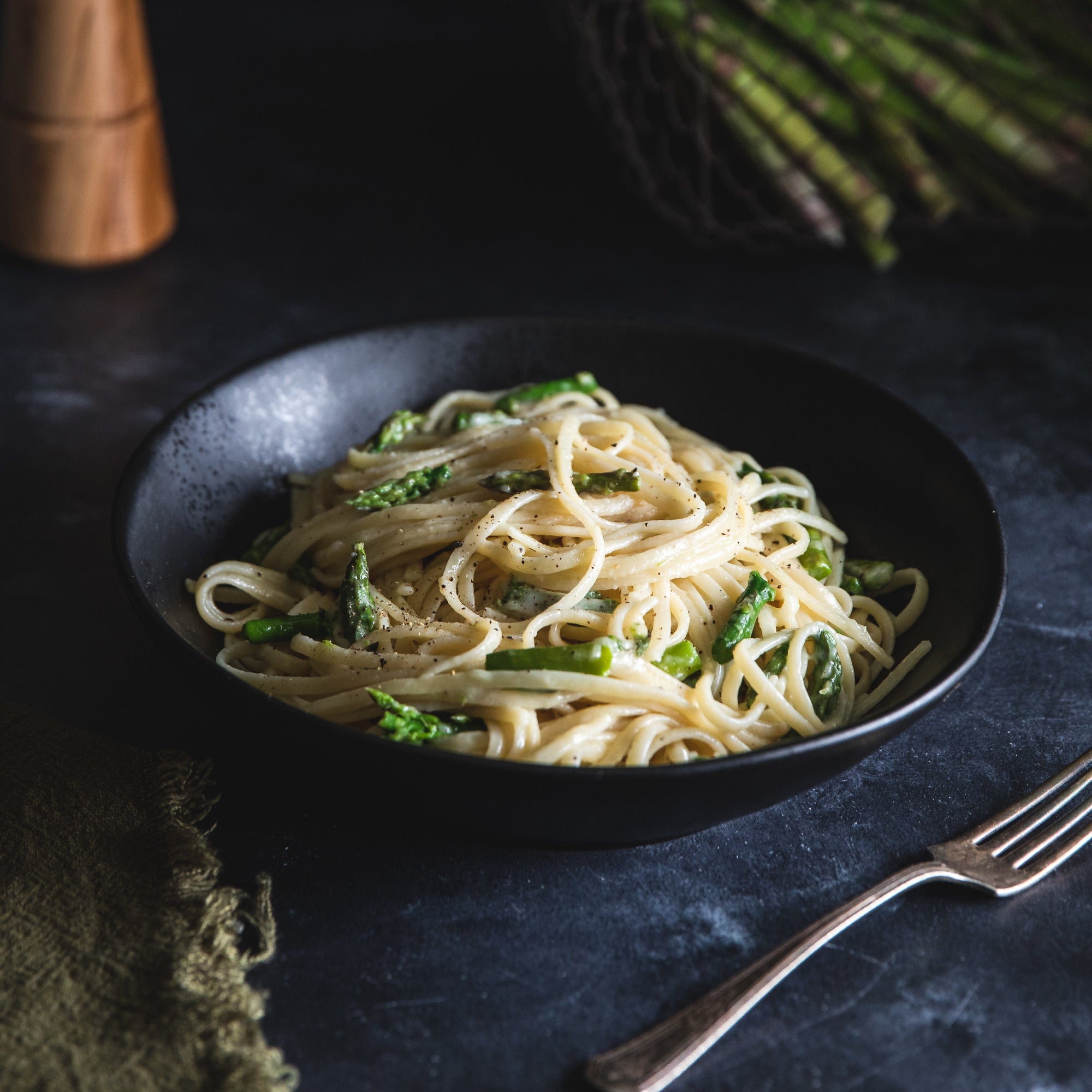 Organic durum semolina linguine tossed with asparagus and cracked black pepper in a black bowl on a dark tabletop