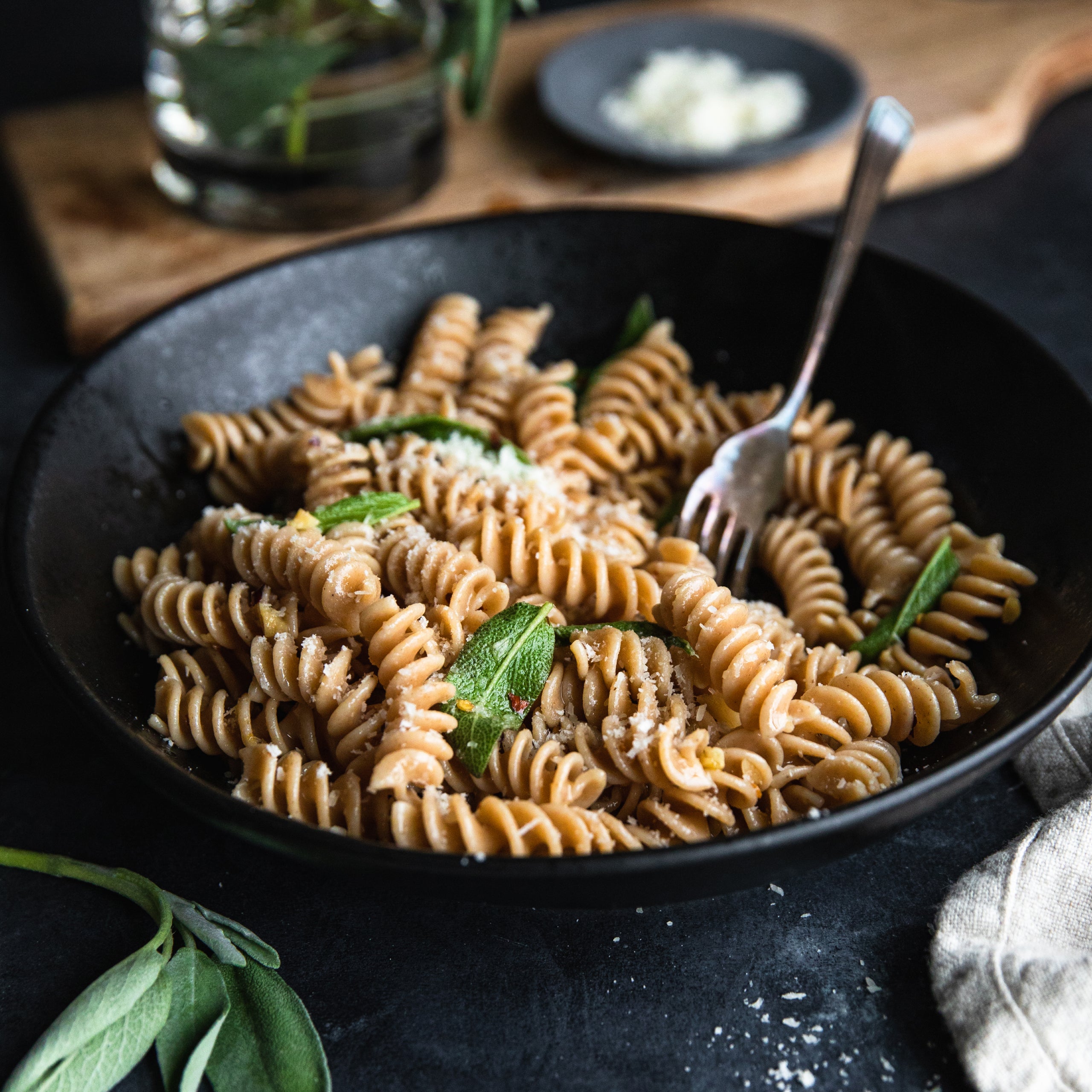 Bowl of cooked Organic Einkorn whole wheat fusilli garnished with basil and a fork on a dark surface