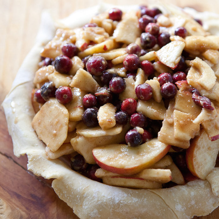 Close-up of unbaked apple cranberry pie in an einkorn crust showing spiced apple slices and whole cranberries on a board