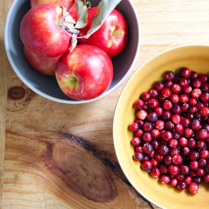 Bowls of red apples and fresh cranberries on a wooden board, ingredients for a spiced apple cranberry pie with einkorn crust