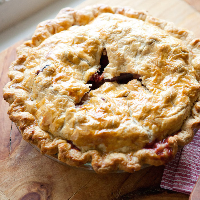 Three-quarter view of spiced apple cranberry pie with golden einkorn crust, flaky crimped edge, and glossy baked top on a wooden board