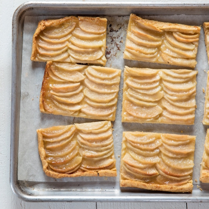 Overhead view of rectangular Einkorn apple caramel tart slices showing layered apple fans on a parchment-lined baking sheet