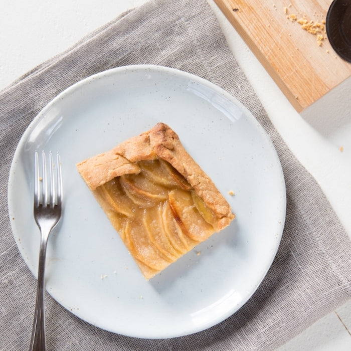 Top-down view of a square slice of einkorn apple caramel tart with layered baked apples and golden crust on a white plate