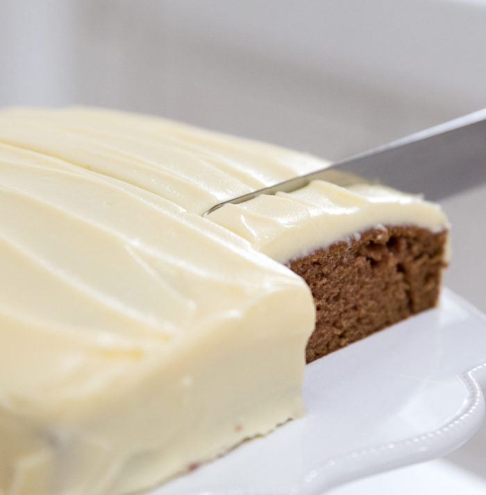 Three-quarter view of Einkorn applesauce spice cake with cream cheese frosting being sliced on a white cake stand