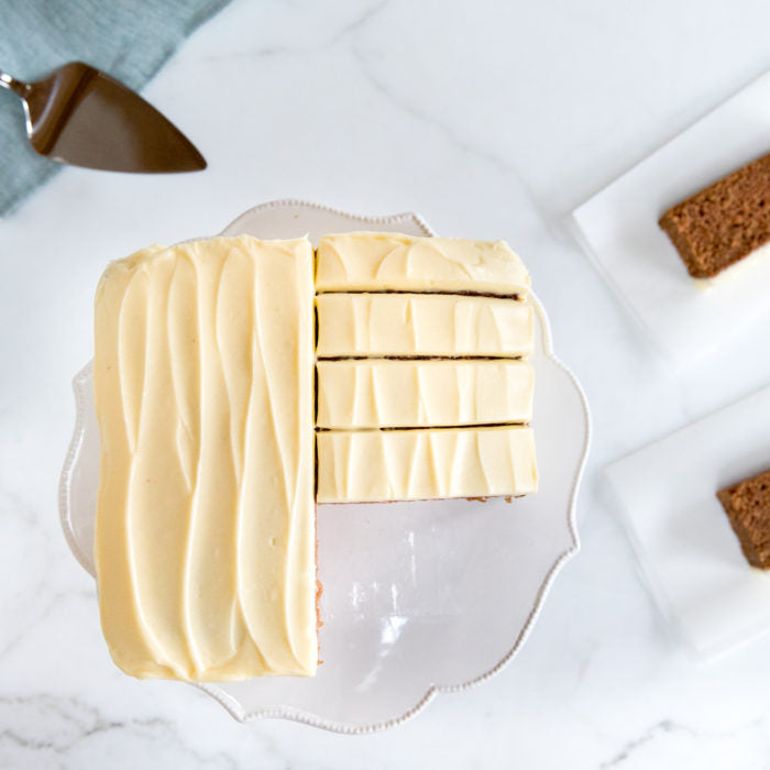 Top-down view of Einkorn applesauce spice cake with pale swirled frosting, sliced into six even pieces on a white cake stand