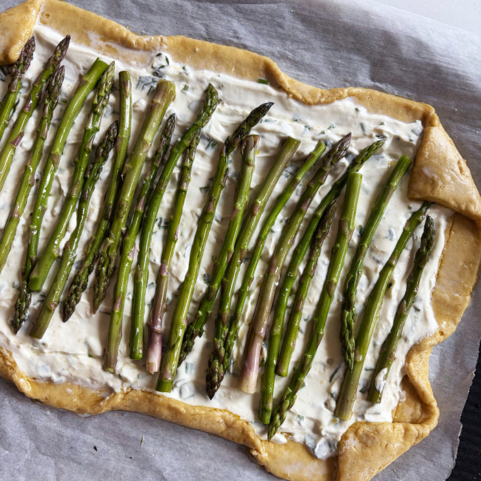 Overhead view of asparagus spring tart with sourdough crust showing asparagus spears on herbed ricotta and folded golden crust on parchment
